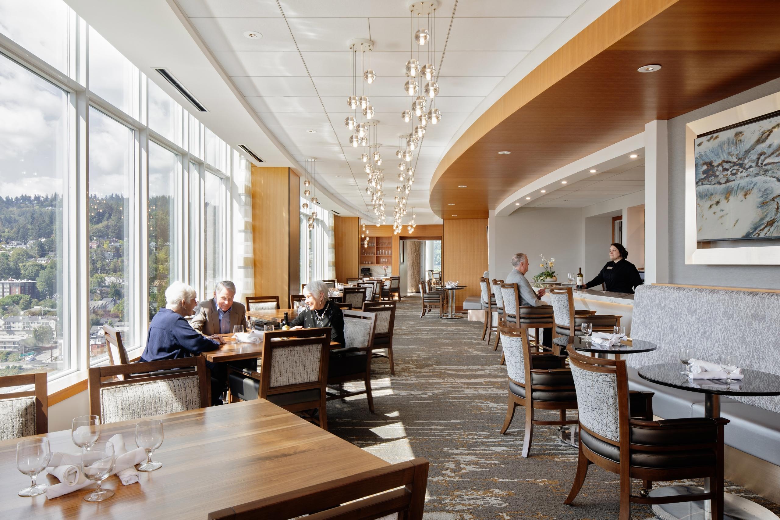 Mirabella Portland dining area. There are two people dining and one resident enjoying a drink at the bar.